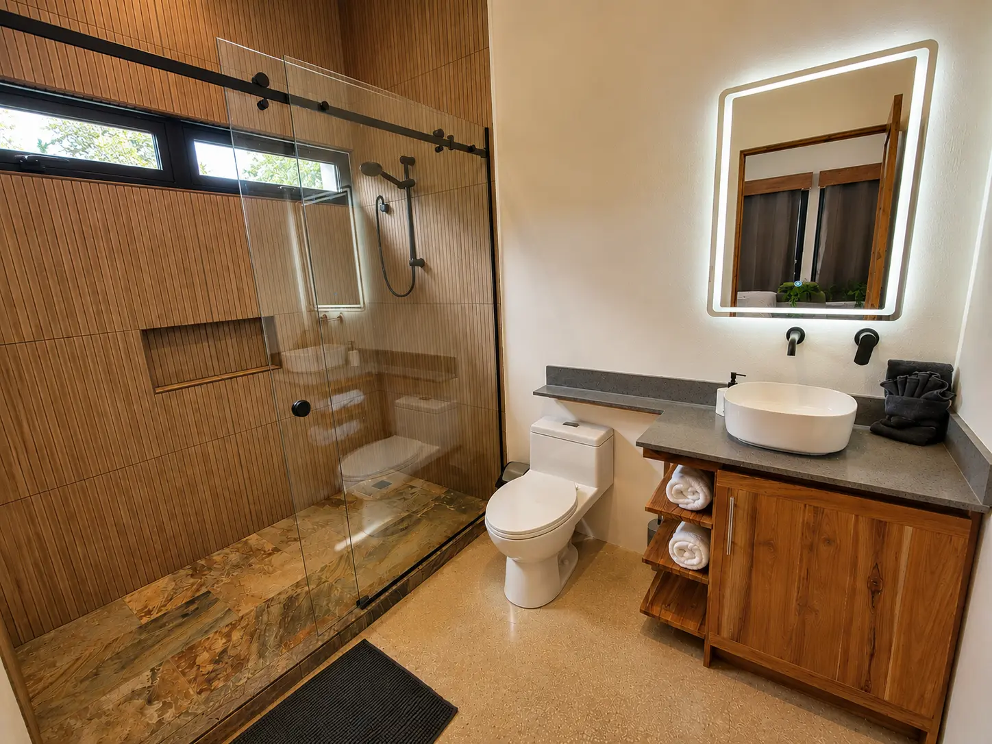 Bathroom with walk-in glass shower, teak vanity and LED-lit mirror
